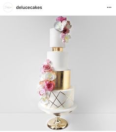 a three tiered cake with flowers on top and gold trimmings is displayed