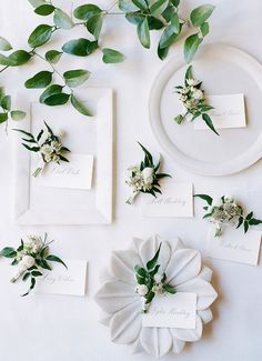 place cards with flowers and greenery are laid out on a white table cloth for an elegant wedding