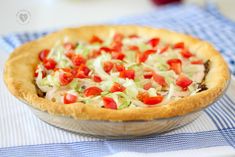 a pie with red and green toppings sitting on top of a blue checkered table cloth