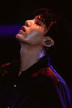 a male in a black shirt and ear piercings is looking up into the sky