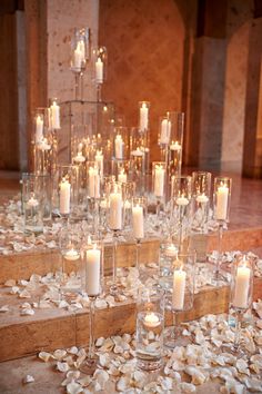 many candles are lit on the floor in front of some glass vases and petals