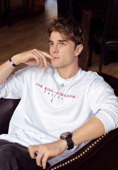 a young man sitting in a chair with his hand on his chin and looking off to the side