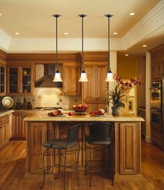 a large kitchen with wooden cabinets and an island in the center is lit by two pendant lights