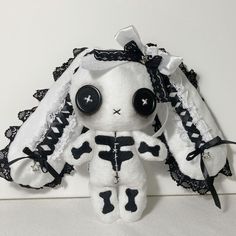 a white stuffed animal with black lace on it's head and eyes, sitting against a white wall