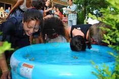 several people are gathered around an inflatable pool with water and plants on the ground