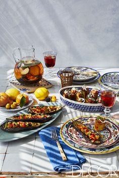 a table topped with plates and bowls filled with food next to glasses of tea on top of a white tile floor