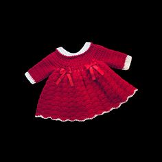 a red knitted dress with white trims and bows on the collar, sitting against a black background