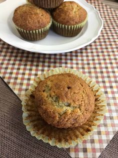 three muffins sitting on top of a checkered table cloth next to a plate