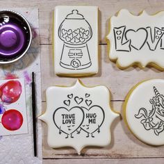 decorated cookies with the words love and two unicorns on them next to a cup of paint