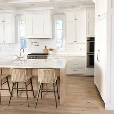 a kitchen with white cabinets and counter tops, two stools at the center of the island