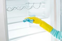 a woman cleaning the inside of a refrigerator with a yellow glove and blue mitt