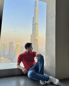 a man sitting on the floor in front of a window looking out at skyscrapers