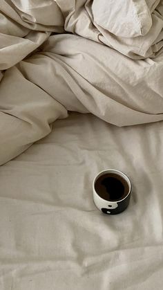 a cup of coffee sitting on top of a bed covered in white sheets and blankets