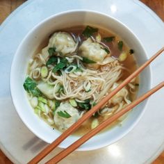 a white bowl filled with soup and chopsticks on top of a wooden table