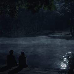 two people sitting on a dock in the dark