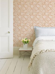 a white bed sitting next to a wall with a flower vase on top of it