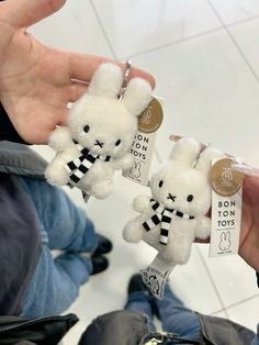 two small stuffed animals are being held by someone's hand in a room with white tile flooring