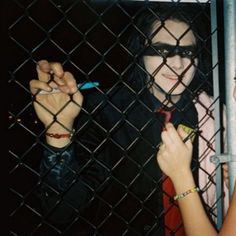 two people behind a chain link fence holding up their hands