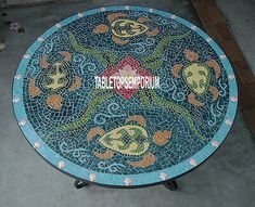 a blue mosaic table with fish and flowers on the top, sitting in front of a building