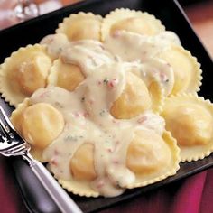 a black plate topped with ravioli covered in gravy next to a fork