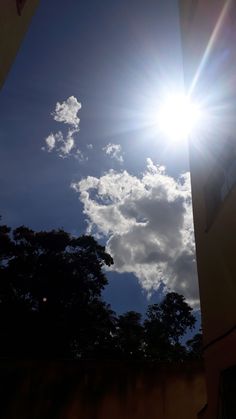 the sun shines brightly in front of some clouds and trees on a sunny day