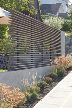 an outdoor area with plants and flowers next to a wall that has a wooden slatted design on it