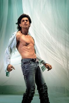 a man with no shirt and jeans standing in front of a curtain