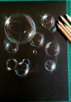 some pencils are laying on top of a drawing board with soap bubbles next to it