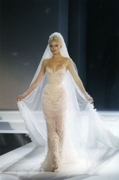 a woman in a wedding dress walking down the runway with a veil on her head