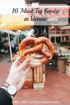 a person holding up a pretzel in front of the camera with text overlay that reads 16 must try foods in vienna