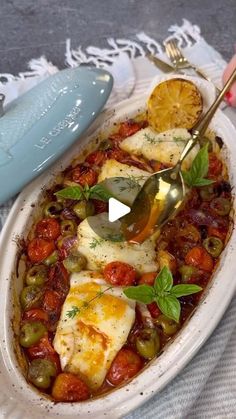 a white bowl filled with food and a spoon on top of a table next to utensils