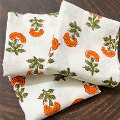 three pieces of cloth with orange flowers on them sitting on top of a wooden table