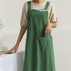 a woman standing next to a white table holding a knife and wearing green aprons