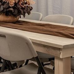 a wooden table topped with a vase filled with flowers next to chairs and a curtain