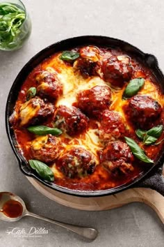 a skillet filled with meatballs covered in cheese and sauce on top of a table