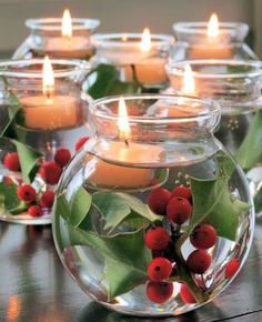 candles are lit in glass vases filled with holly and red berries