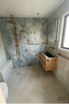 a bathroom with marble walls and flooring in the shower area, along with a wooden cabinet