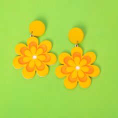 two pairs of yellow and orange flower shaped earrings on green background with copy space for text