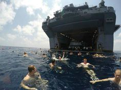 people swimming in the ocean near an aircraft carrier