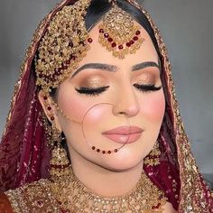 a woman in a red and gold bridal outfit with her nose ring on top of her head