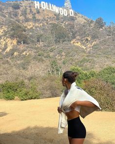 a woman is standing in front of the hollywood sign with her jacket over her shoulders