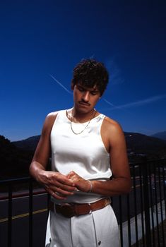 a man standing next to a fence looking at his cell phone while wearing a white dress