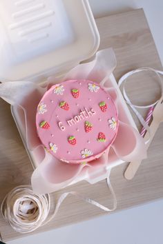 a pink cake with strawberries on it sitting in a box next to some scissors