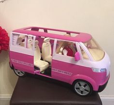 a pink toy van with its doors open on a table next to a red flower