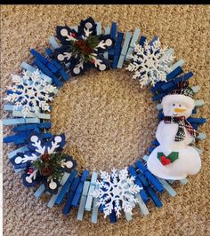 a snowman wreath made out of popsicle sticks on the floor with christmas decorations around it