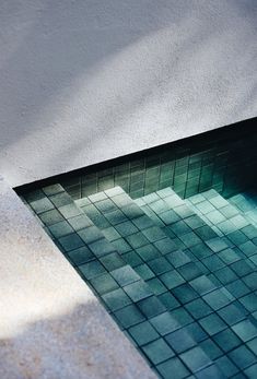 the reflection of an umbrella on top of a tiled swimming pool in a concrete wall