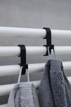 two towels are hanging on the wall next to a towel rack with black handles and hooks