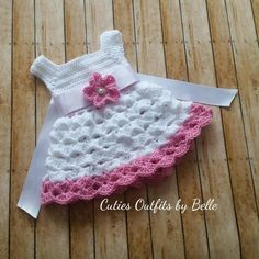 a white and pink crocheted dress laying on top of a wooden floor