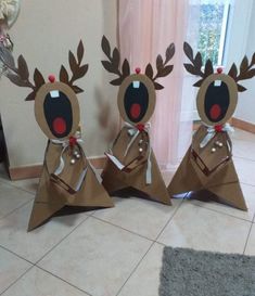 three brown paper christmas decorations with red noses and antlers on them, sitting in front of a window