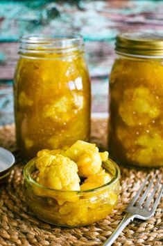 two jars filled with food sitting on top of a woven place mat next to a fork